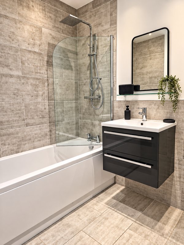 Modern bathroom with white bathtub, glass shower enclosure, dark vanity unit and mirror