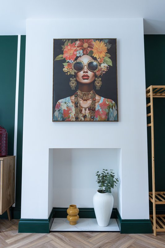 White wall niche with potted plant, framed portrait art, and decorative gold candles