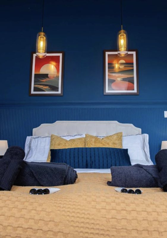 Modern bedroom with blue wall, framed artwork, pendant lights, and gold accent pillow