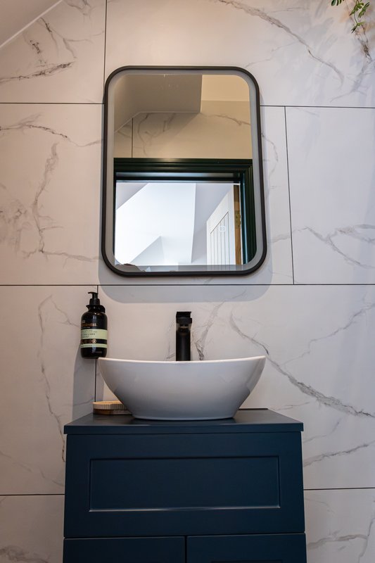 Modern bathroom with white vessel sink, dark blue vanity, and framed mirror above
