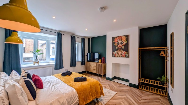 Spacious bedroom with double bed, gold pendant lamp, wooden floor and green accent wall