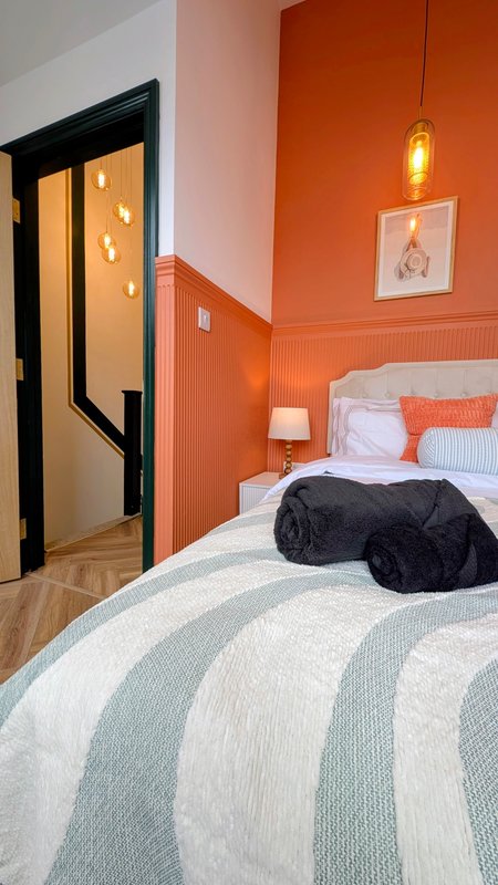 Bedroom with orange walls, striped bedding, pendant light, and open doorway