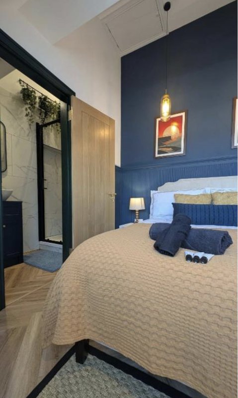 Modern bedroom with blue feature wall, double bed, wooden door and contemporary lighting