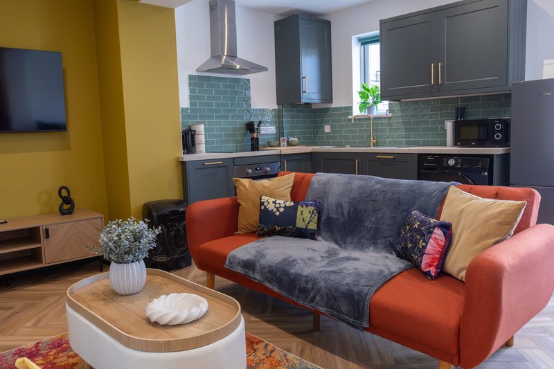 Open-plan kitchen and living room with orange sofa, wooden coffee table, and green tile backsplash