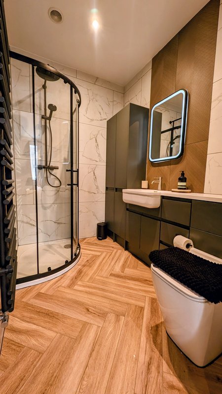 Modern bathroom with curved shower enclosure, vanity sink, illuminated mirror and wooden flooring