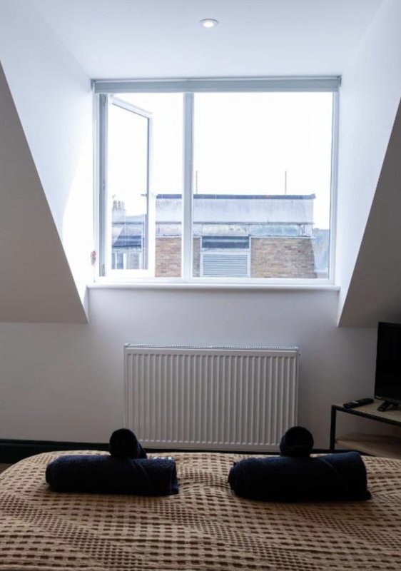 Bright attic room with skylight window, radiator, and black floor cushions on patterned rug