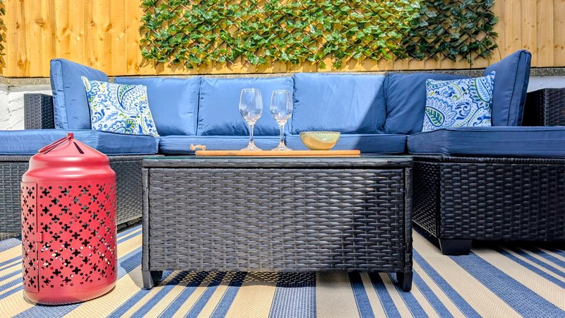 Outdoor patio seating area with blue cushioned sofa, black wicker table, and decorative lantern