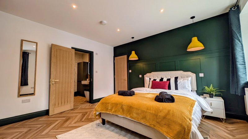 Modern bedroom with double bed, yellow throw, dark green accent wall and wooden flooring
