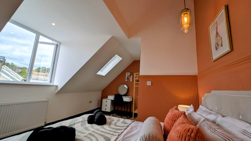 Bright attic bedroom with sloped ceiling, double bed, orange accent wall and skylight window