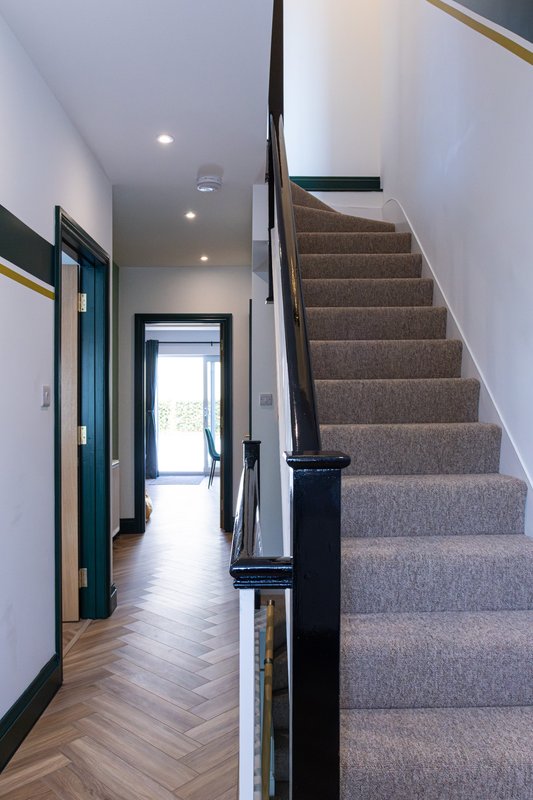 Modern hallway with staircase, wooden flooring, white walls and black railing
