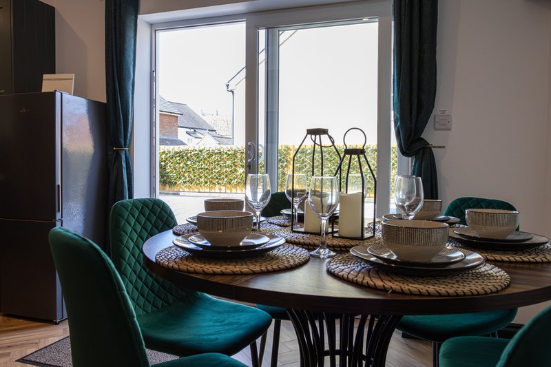Dining room with round dark table, teal velvet chairs, place settings and garden view through patio doors