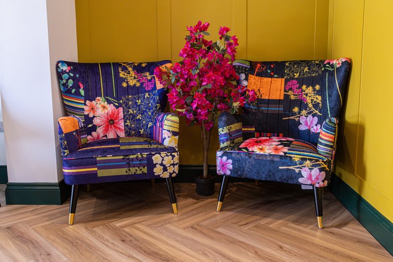 Two floral-patterned armchairs with pink flowers in vase between them, yellow wall background