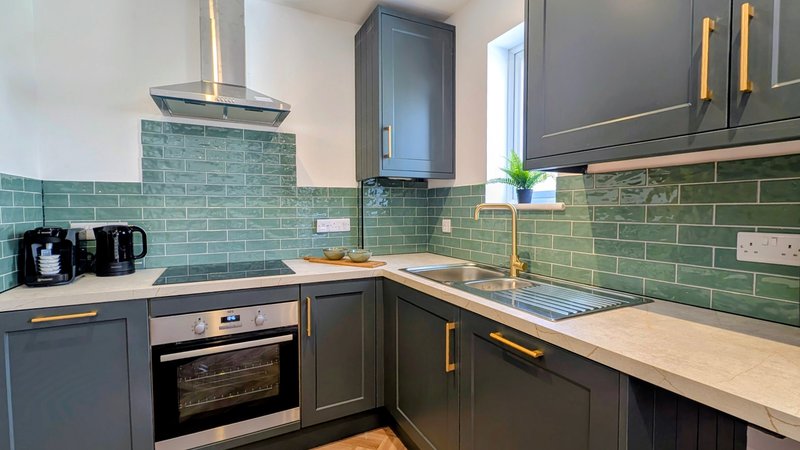 Modern kitchen with dark cabinetry, green subway tile backsplash, and stainless steel appliances