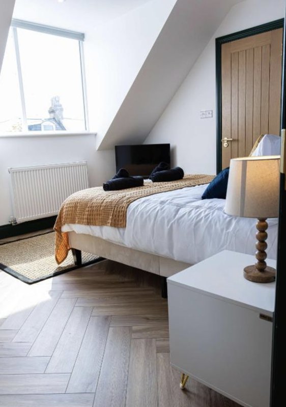 Bright attic bedroom with double bed, TV, white dresser, and sloped ceiling with window