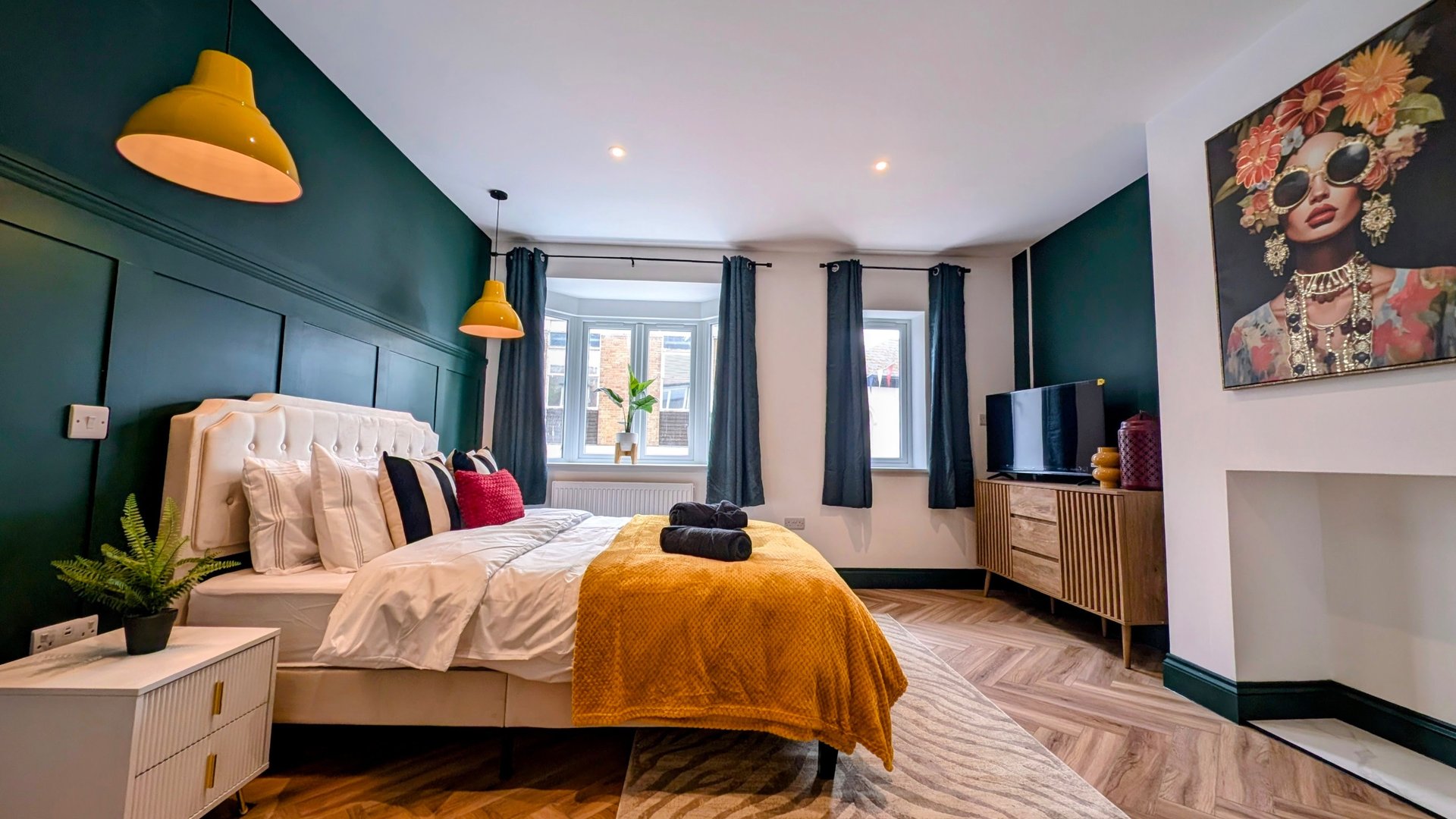 Modern bedroom with teal walls, double bed, yellow pendant lights and contemporary artwork