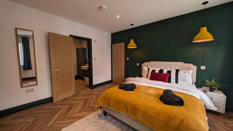 Modern bedroom with double bed, yellow bedding, dark green accent wall, pendant lights and wooden flooring
