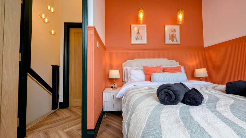 Modern bedroom with orange accent wall, white bed, pendant lights, and wooden flooring