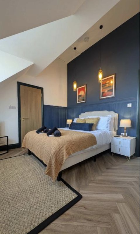 Modern bedroom with double bed, blue feature wall, pendant lights and angled ceiling
