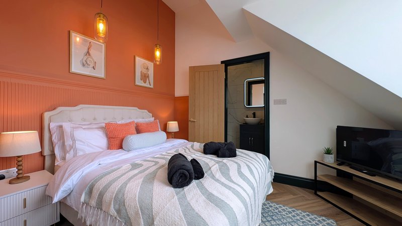 Attic bedroom with double bed, orange accent wall, pendant lights and ensuite bathroom door