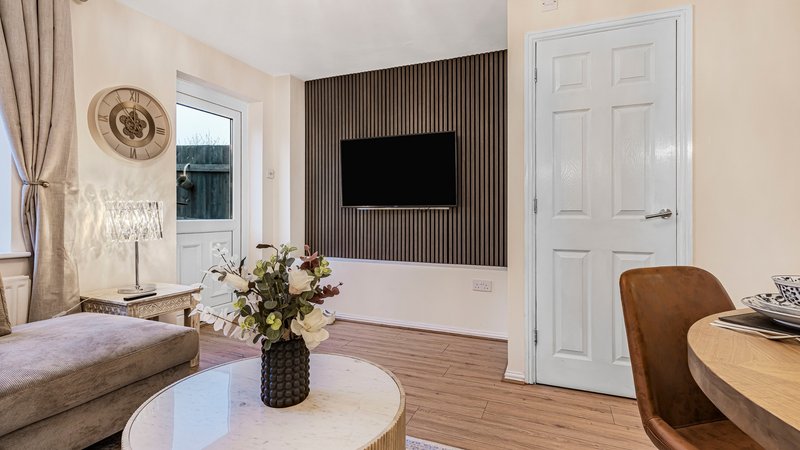Modern living room with wall-mounted TV, round white coffee table, upholstered seating, and floral arrangement