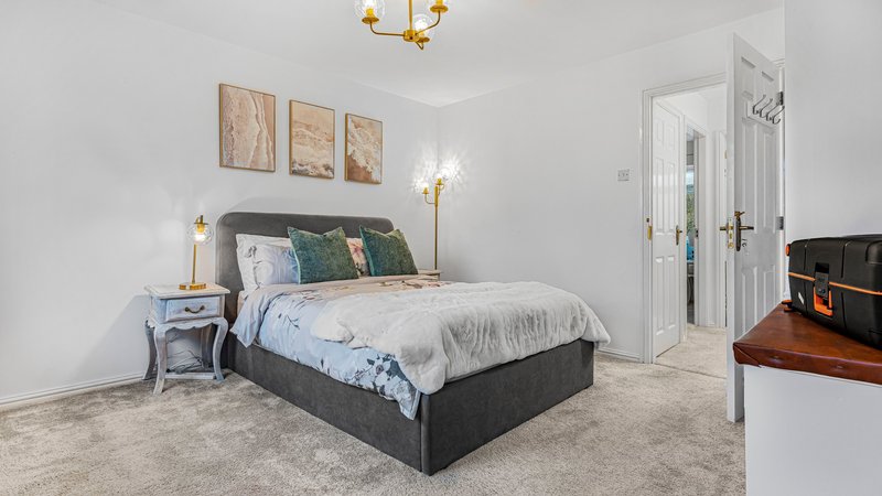 Bright bedroom with queen bed, bedside tables, wall art, and ensuite bathroom entrance