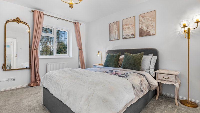 Bedroom with double bed, ornate mirror, window with pink curtains, and wall art