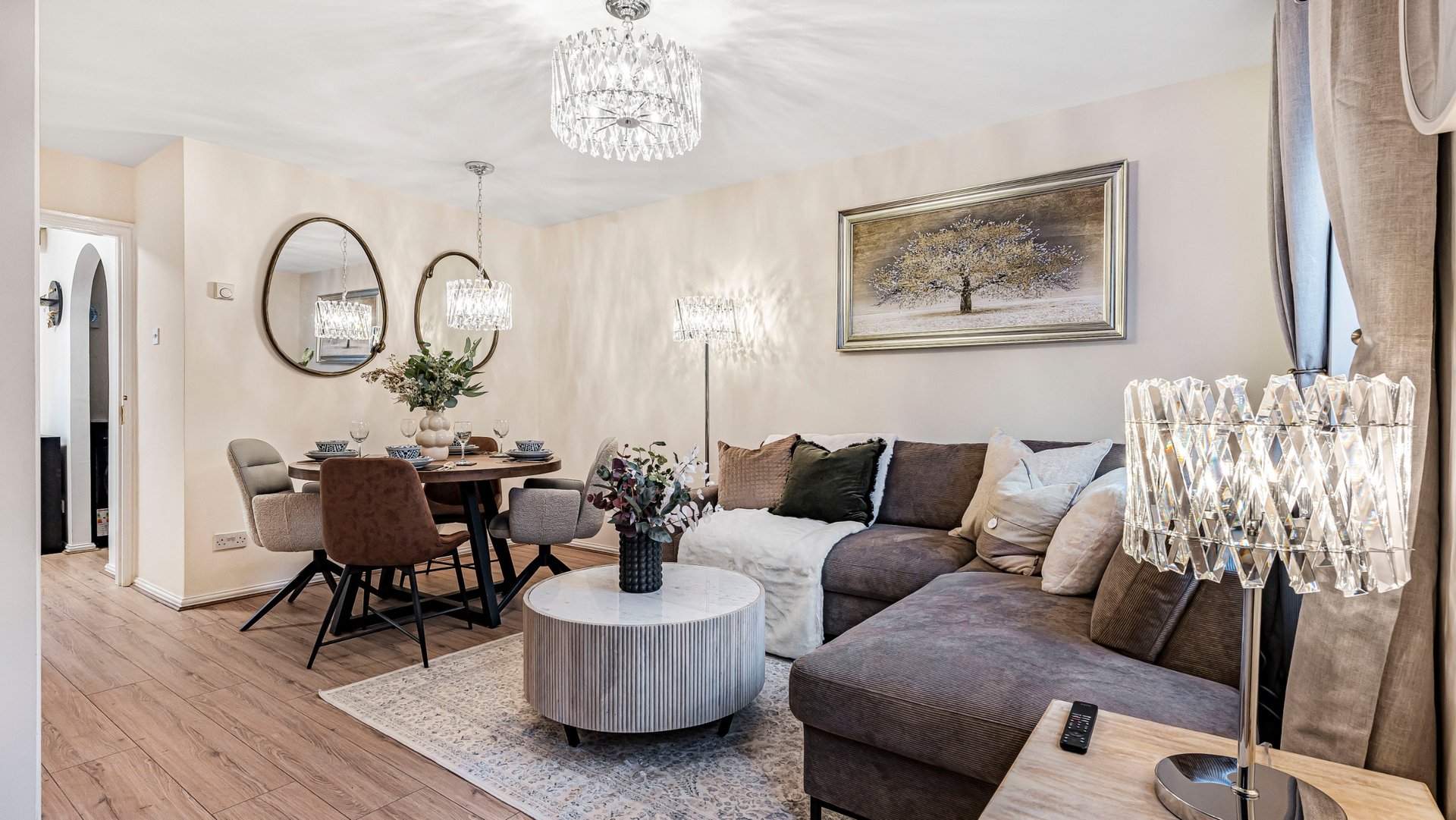 Open-plan living area with grey sofa, dining table, round coffee table and crystal chandelier