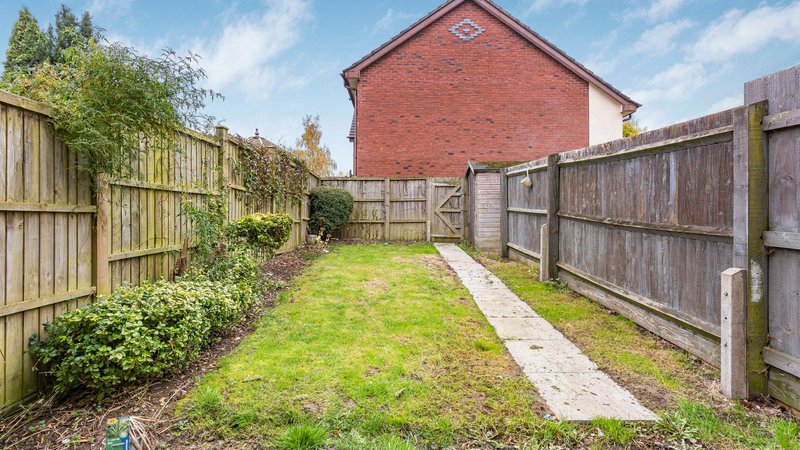 Rear garden with lawn, wooden fences, brick house, and pathway