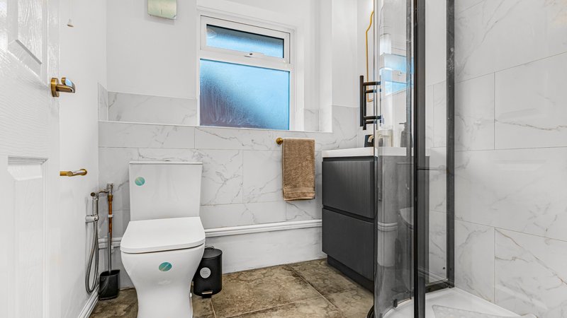 Modern bathroom with white toilet, marble tile walls, window, and dark shower enclosure