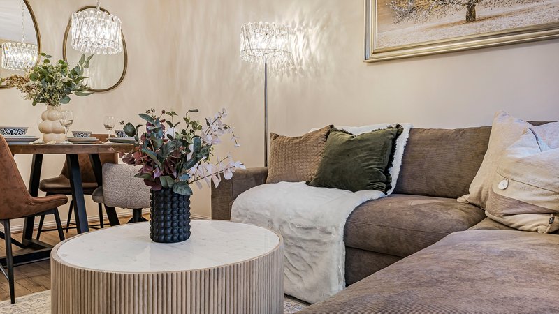 Modern living room with sofa, round table, flowers, pendant lights and dining area