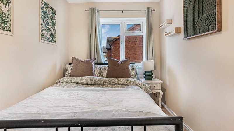 Bright bedroom with double bed, brown pillows, window with curtains and brick view