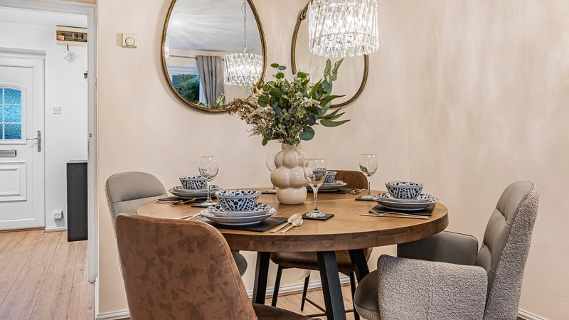 Dining room with round wooden table, upholstered chairs, and modern pendant light fixture