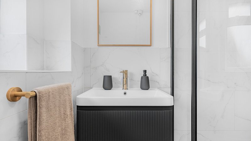 Modern bathroom with white marble tiles, black vanity unit, and brass fixtures