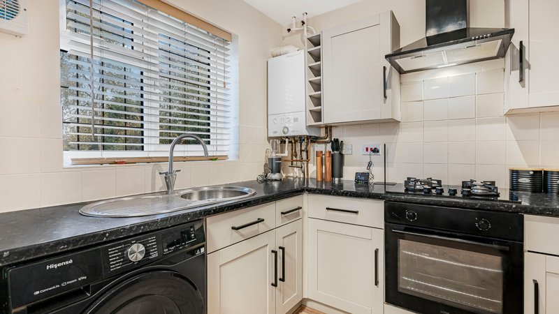 Modern kitchen with cream cabinets, black countertop, integrated appliances and window with blinds