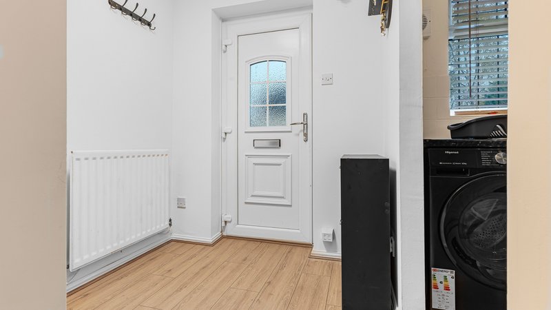 Hallway with white door, wooden floor, radiator and black washing machine