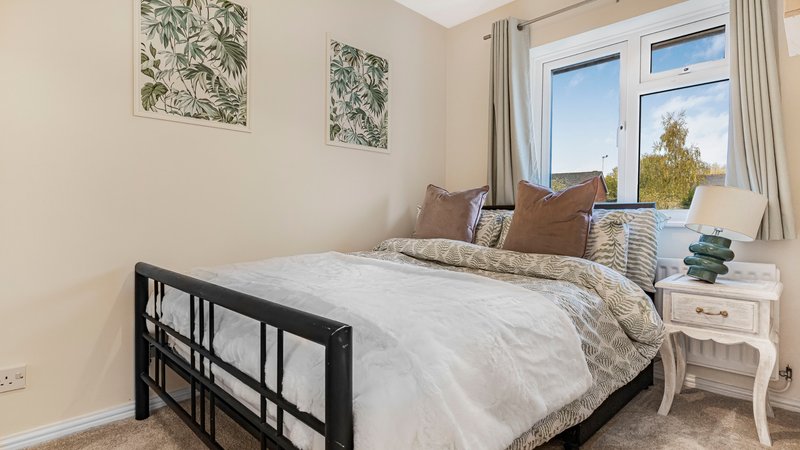 Bright bedroom with black metal bed frame, white bedding, brown cushions, and large windows with natural light