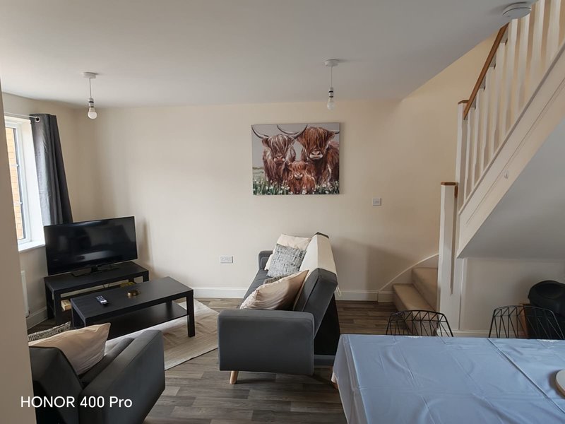 Open-plan living room with grey armchair, TV, stairs, and framed wall art