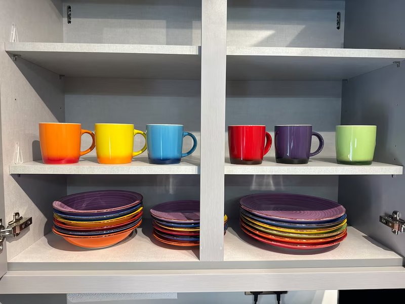 White kitchen shelving unit displaying colorful ceramic mugs and stacked plates