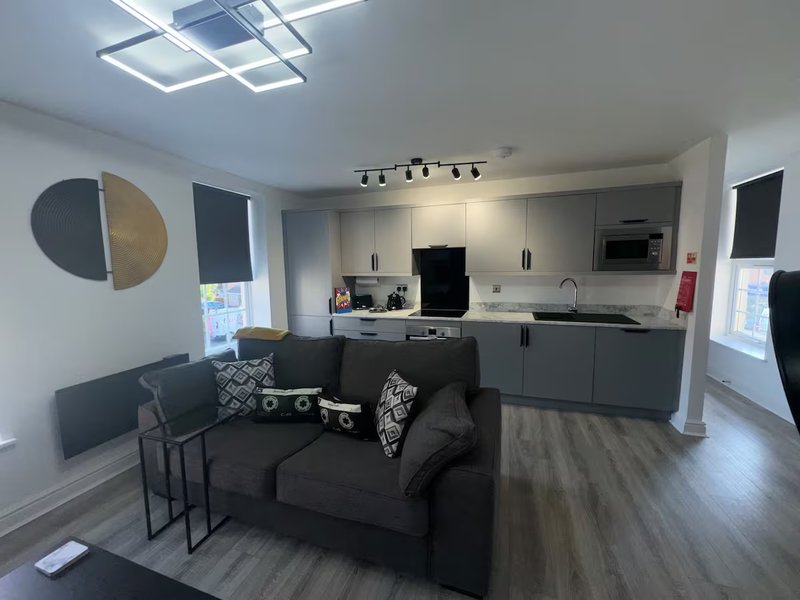 Open-plan living room and kitchen with black sofa, dining table, and modern fitted kitchen