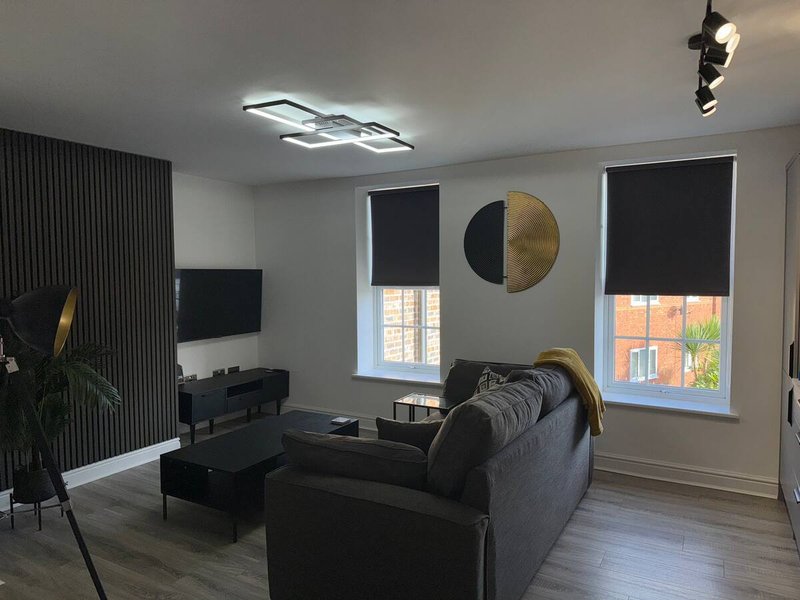 Modern living room with black sofa, TV stand, geometric wall art and large windows