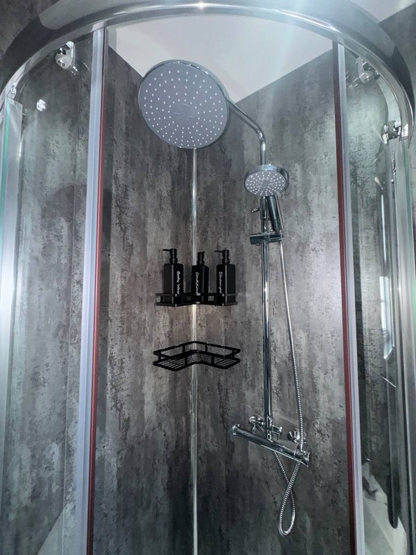 Modern shower enclosure with rainfall showerhead, black fixtures and dark tiled walls