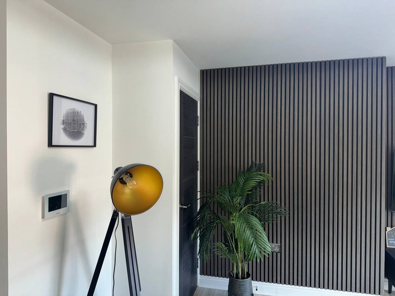 Modern bedroom corner with white walls, black tripod lamp, framed artwork, and potted plant