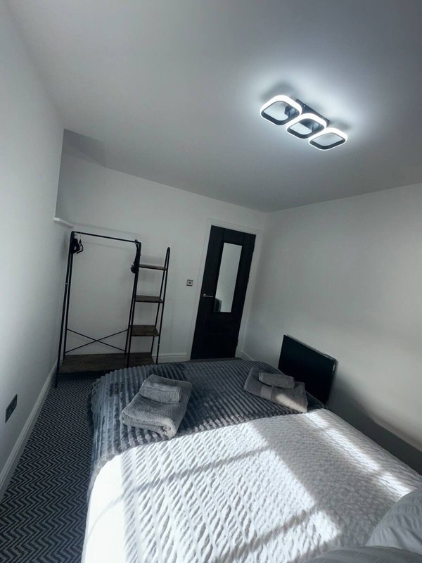 Modest bedroom with single bed, clothing rack, black door and ceiling light fixture