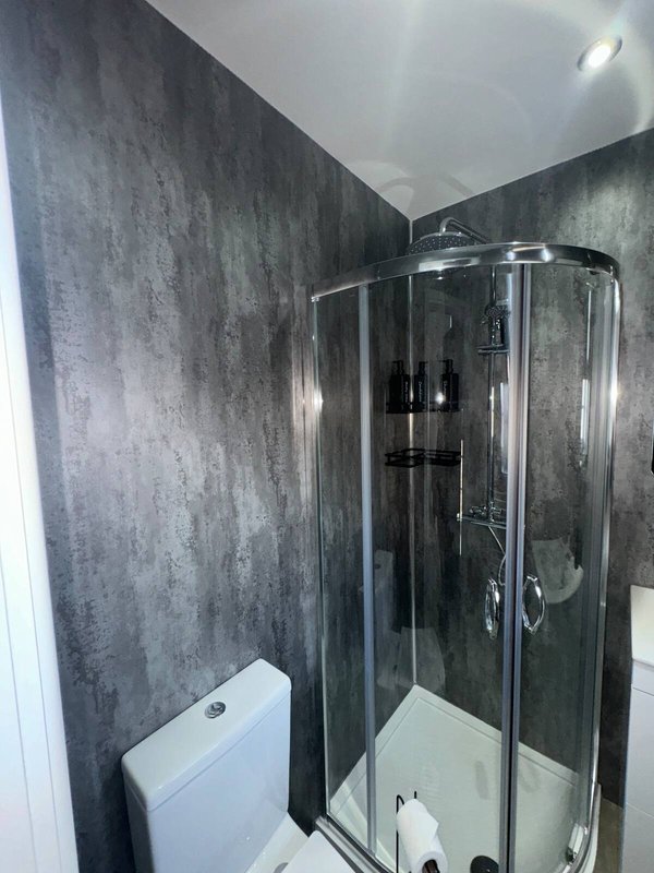 Modern bathroom with dark tiled walls, enclosed shower cubicle and white toilet