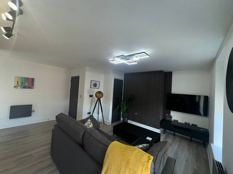 Modern living room with grey sofa, yellow throw, flat-screen TV, tripod lamp and wooden flooring