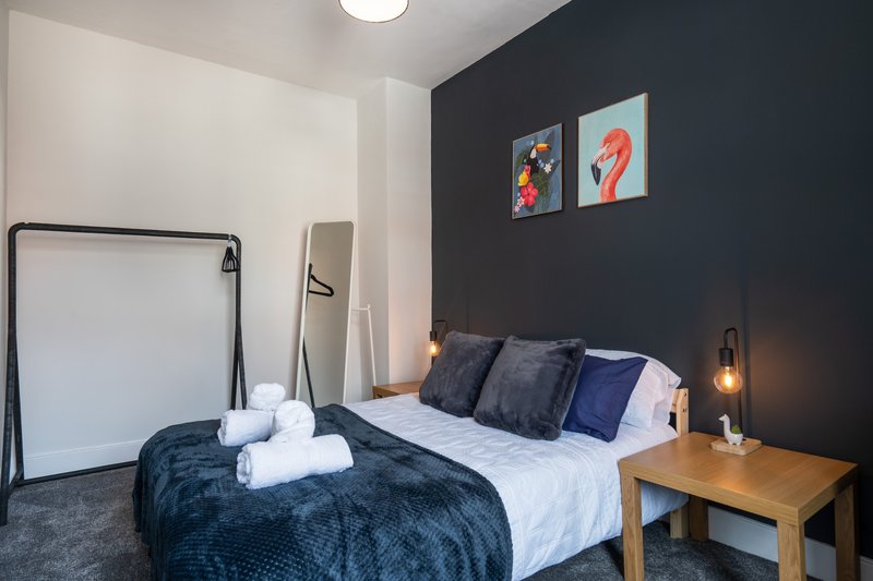 Modern bedroom with double bed, dark feature wall, bedside table and framed artwork