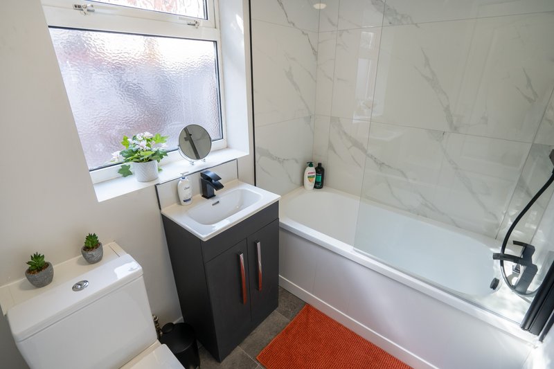 Modern bathroom with white marble tiles, black vanity, bathtub, and small potted plants