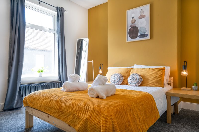 Bright bedroom with mustard yellow walls, wooden bed frame, white pillows and golden bedding