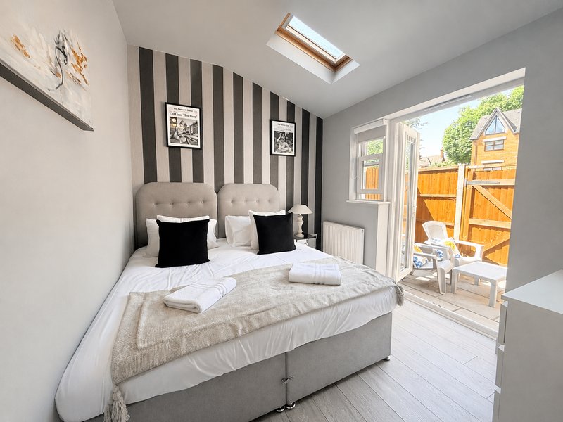 Modern bedroom with striped accent wall, double bed with black cushions, skylight and patio doors to garden.