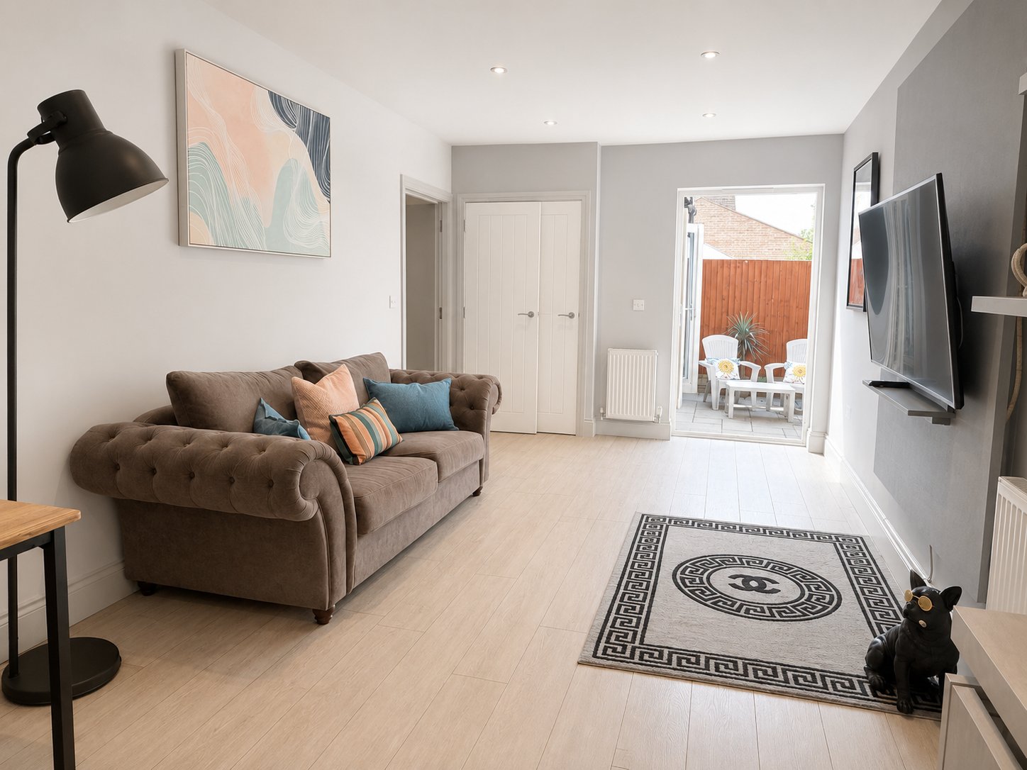 Modern living room with brown chesterfield sofa, wooden floor, wall-mounted TV, and patio doors